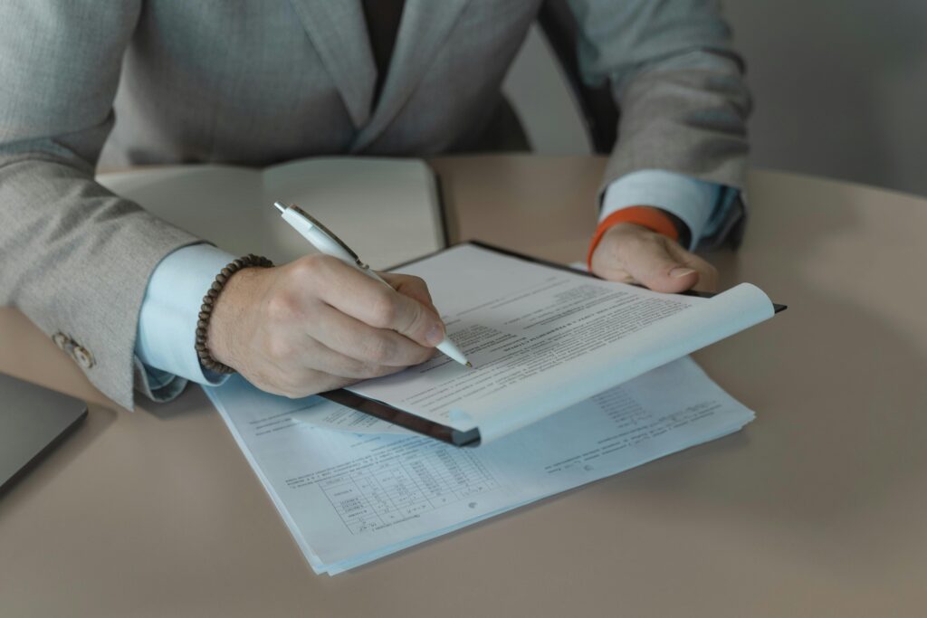 Close-up of business person signing documents at a desk with a pen.